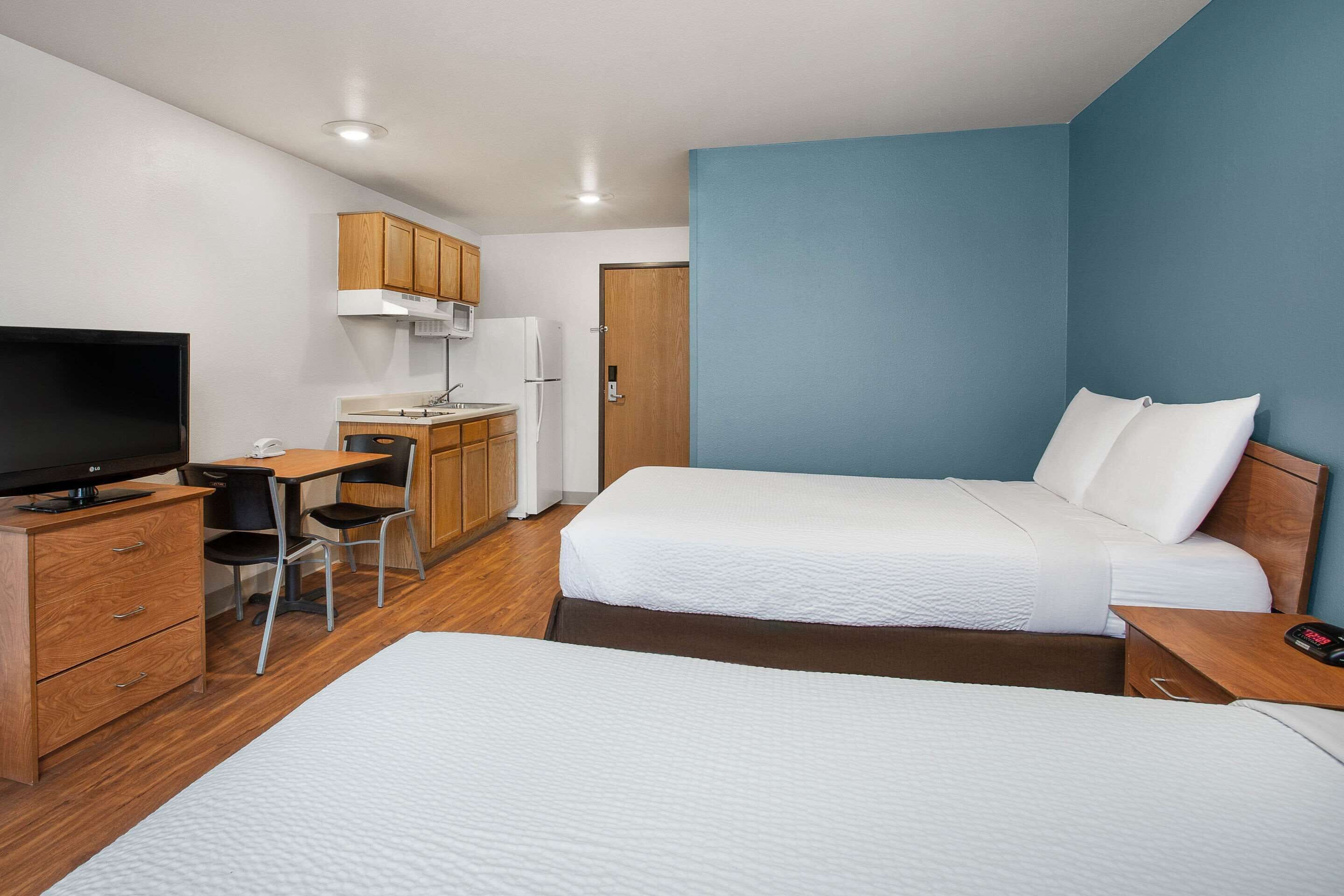 Una camera d'albergo con un letto, una scrivania con una sedia, una televisione e un angolo cottura.