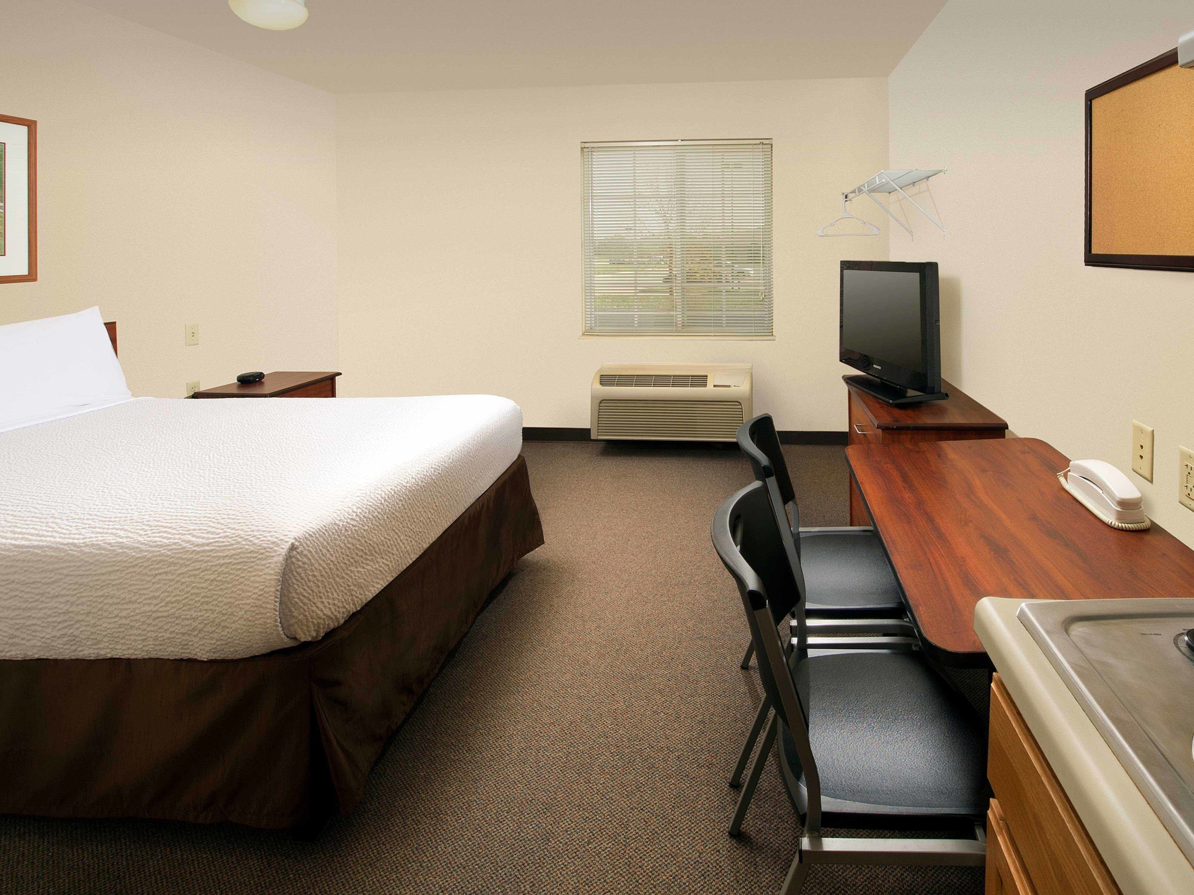 A hotel room with a bed, a desk with a chair, a television, and a heater.