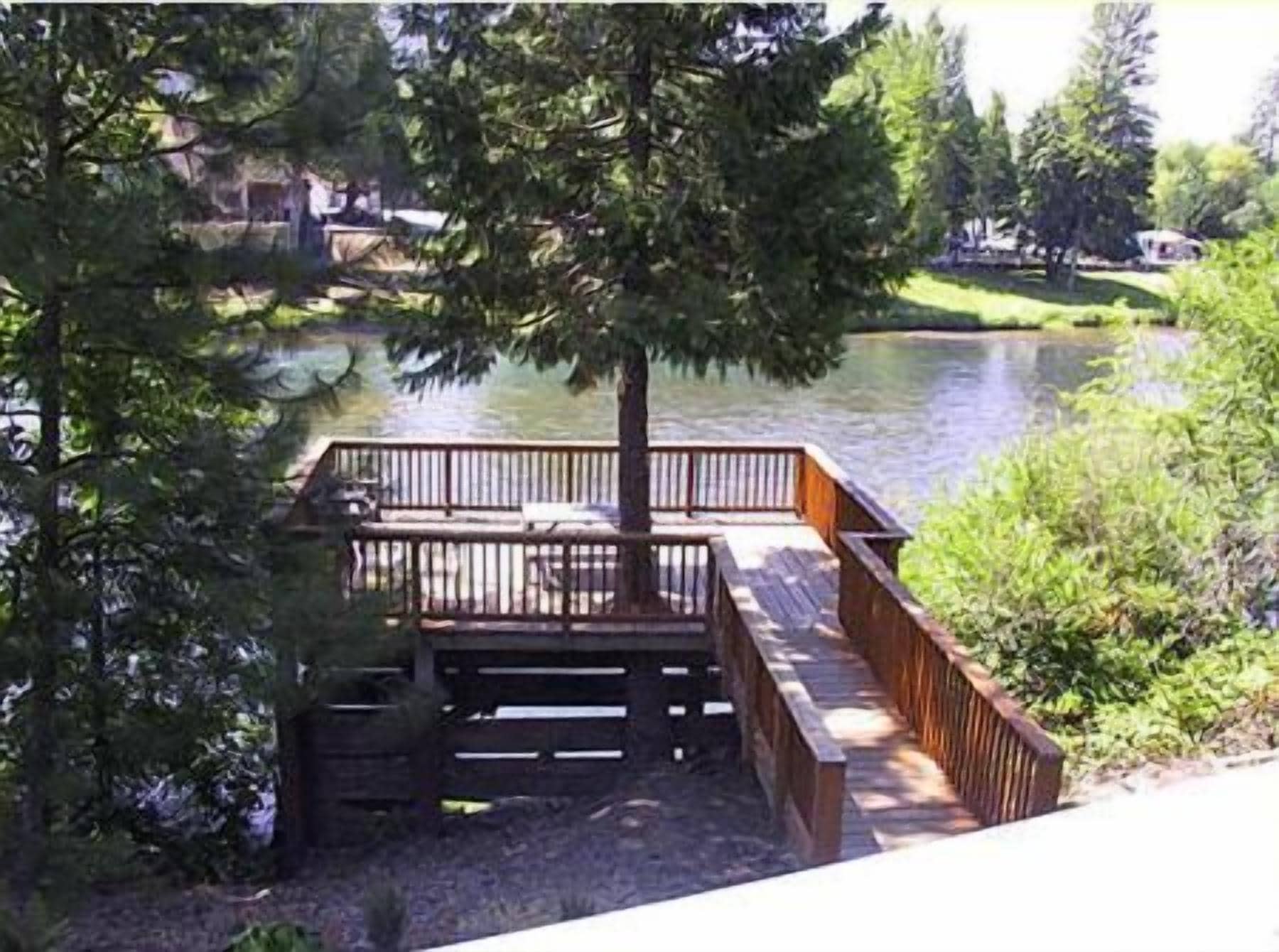A wooden deck with a railing overlooking a body of water, surrounded by trees and vegetation.