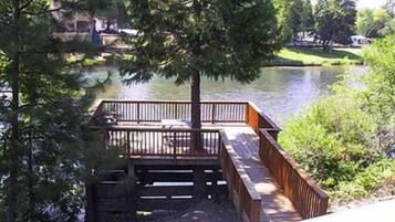 Une terrasse en bois, dotée d’une balustrade, qui surplombe une étendue d’eau et est entourée d’arbres et de végétation.