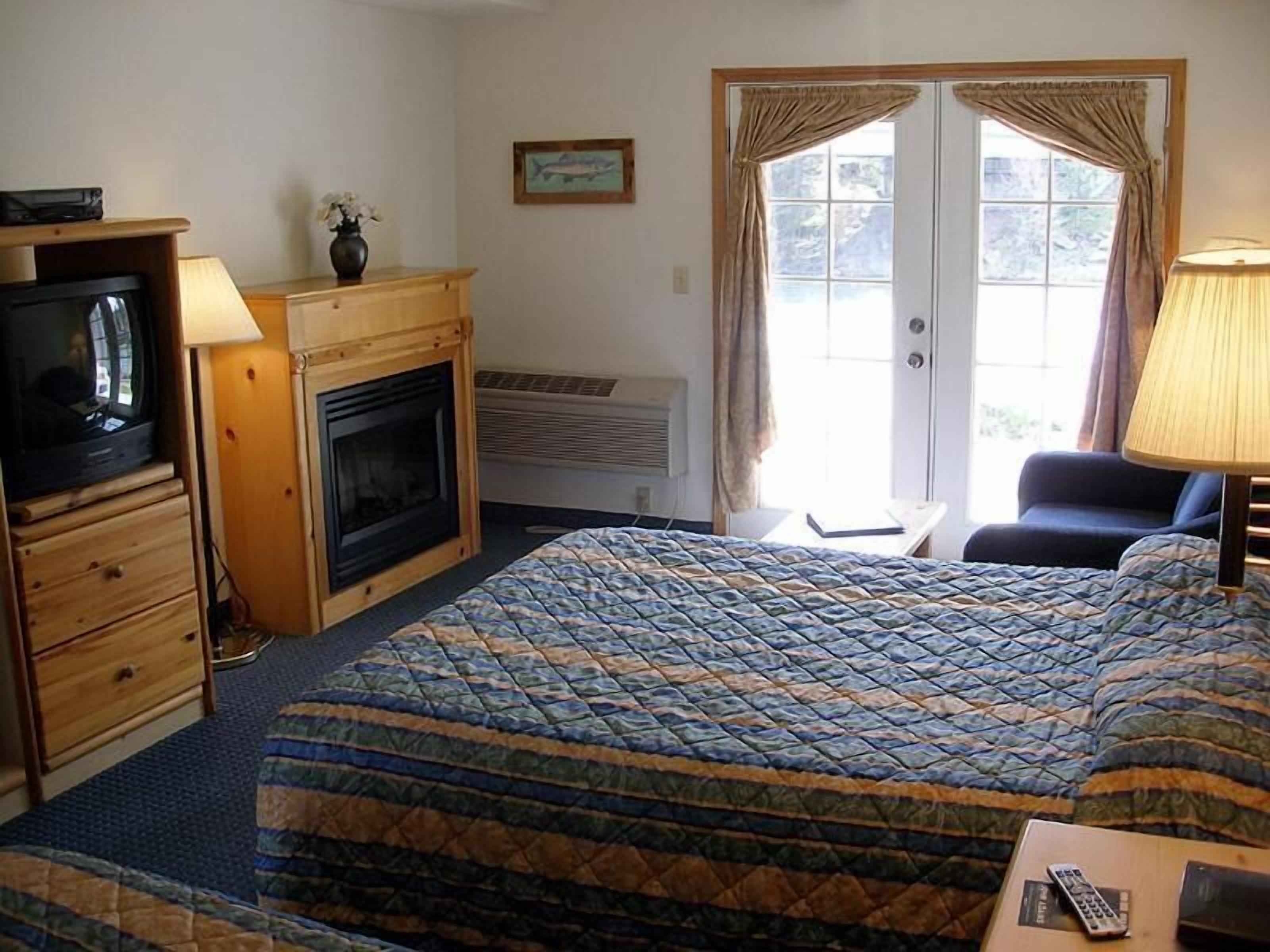 Una habitación de hotel con cama, televisión, chimenea, escritorio y una silla.