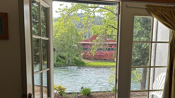 A room with a large glass door leading to a patio with a view of a lake and a building with red roofs. - Edgewater Inn Shady Cove (Shady Cove)