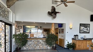 A reception area with a stone wall, wooden reception desk, potted plants, and a ceiling fan. - Edgewater Inn Shady Cove (Shady Cove)