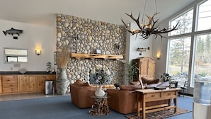 A spacious living room with a stone wall, a large chandelier, and a view through a window. - Edgewater Inn Shady Cove (Shady Cove)