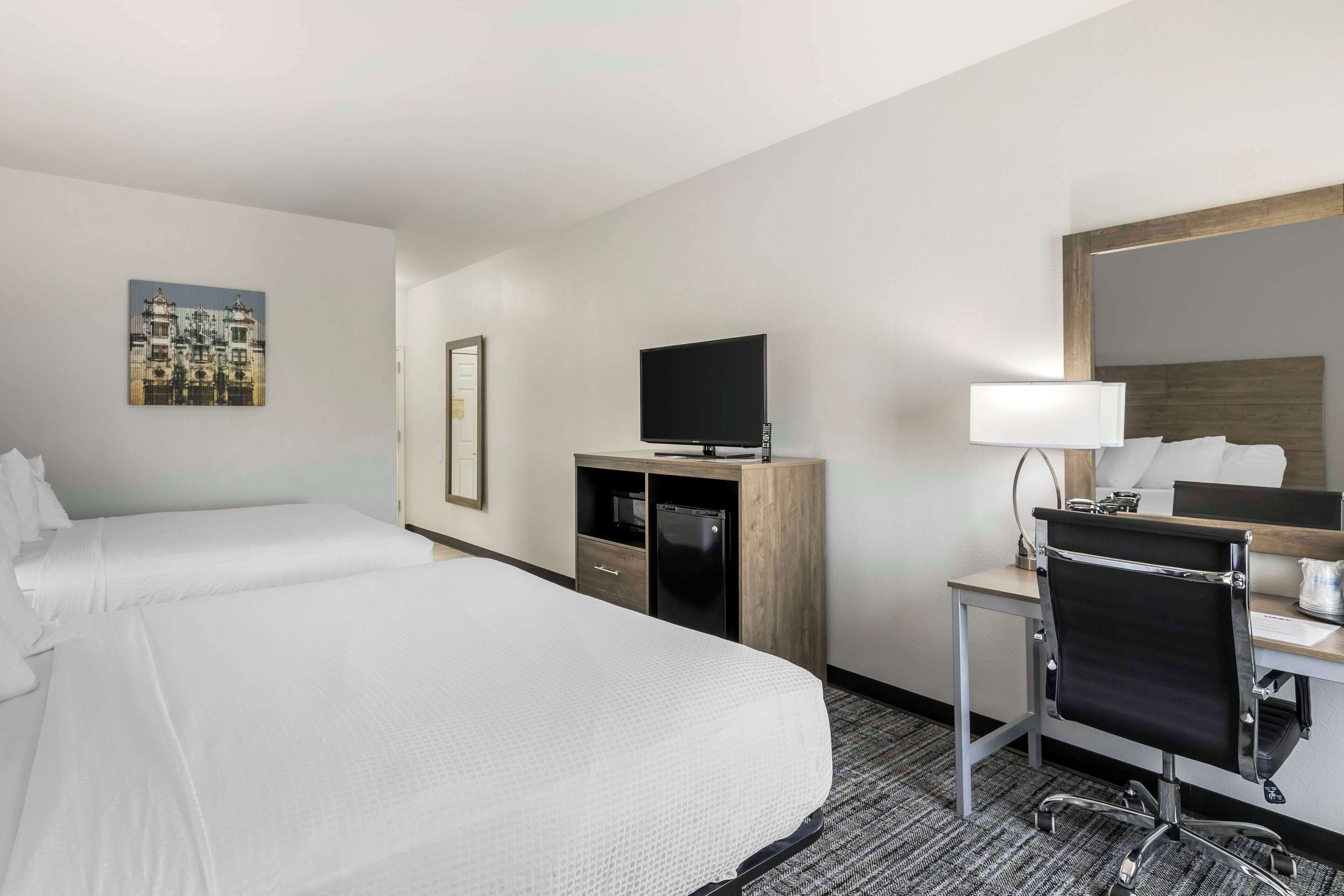 A hotel room with two beds, a desk with a chair, a television, and a mirror.