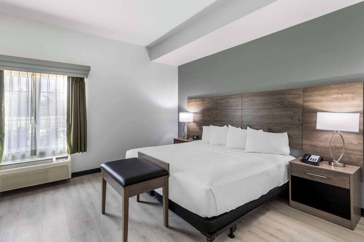 A modern hotel room with a large bed, bedside tables, a desk, and a window with curtains.