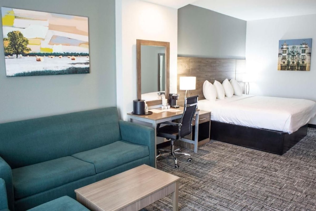 A hotel room with a bed, a desk with a chair, a sofa, a coffee table, and a mirror.