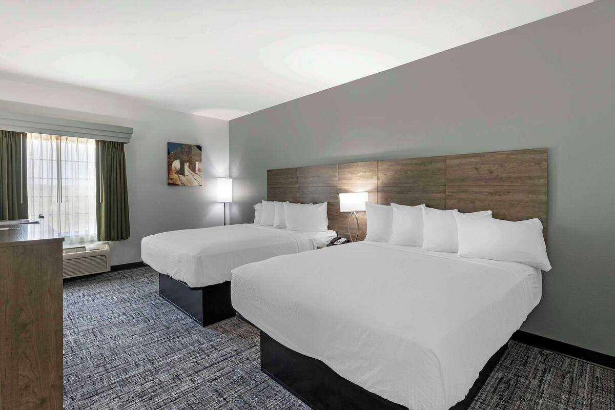 A hotel room with two beds, a desk, and a window with curtains.