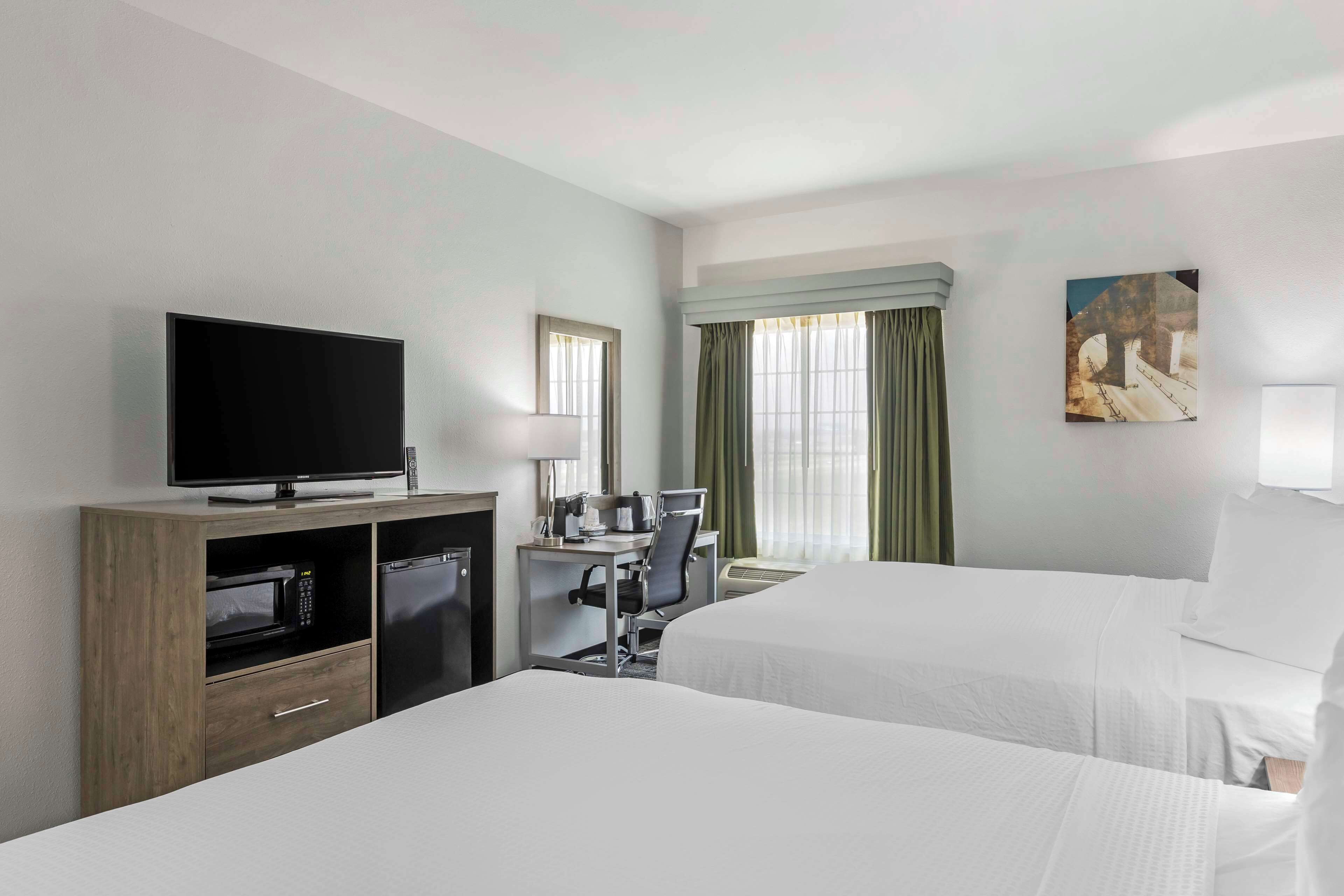 Une chambre d’hôtel avec deux lits, une télévision, un bureau avec une chaise, un four à micro-ondes et un petit placard.