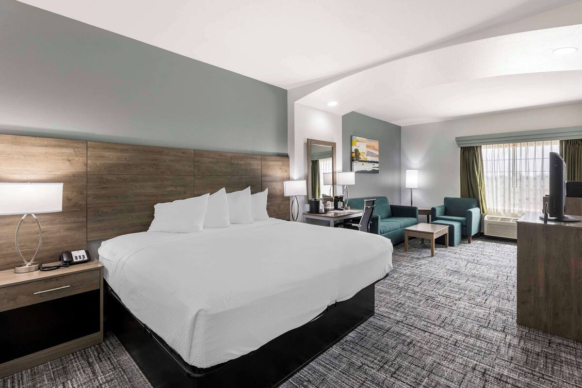 A hotel room with a large bed, a desk with a chair, a sofa, and a TV.