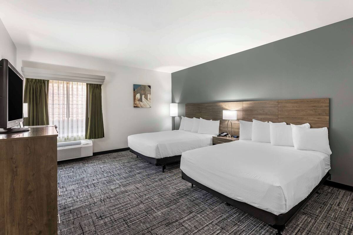 A hotel room with two beds, a desk, a TV, a window with curtains, and a painting on the wall.