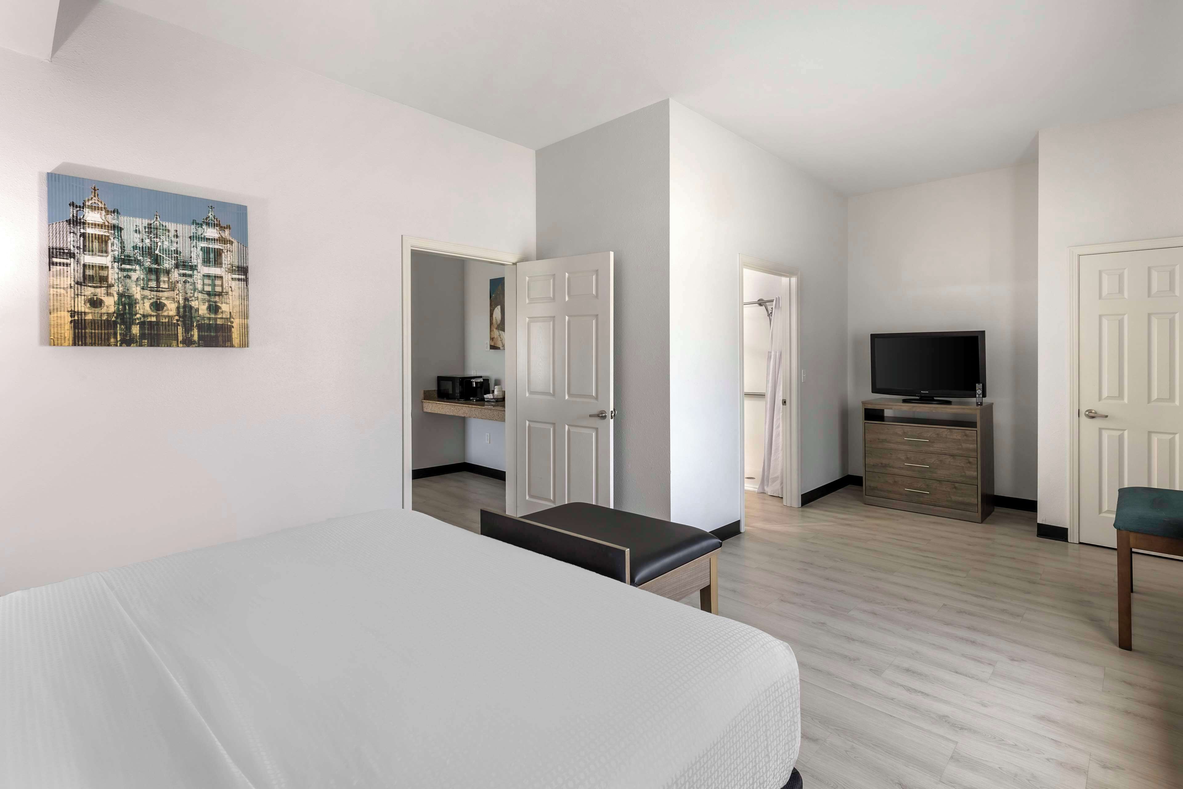 Habitació d'hotel moderna amb un llit, una televisió, una taula de treball i un bany visible a través d'una porta oberta.