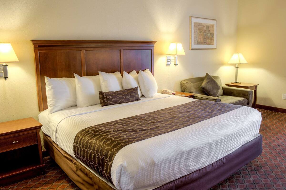 A hotel room with a large bed, two bedside tables, a chair, and two wall-mounted lamps.