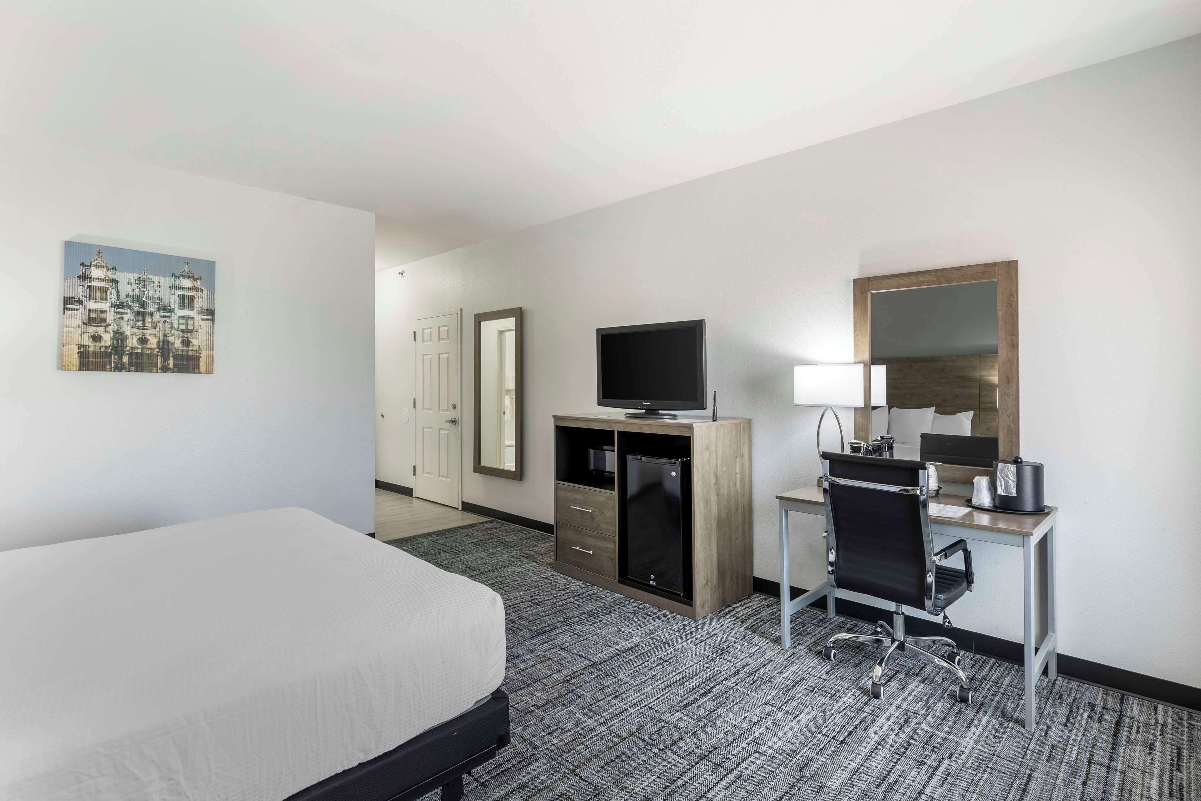 Una habitación de hotel con cama, escritorio, computadora, televisor y espejo.