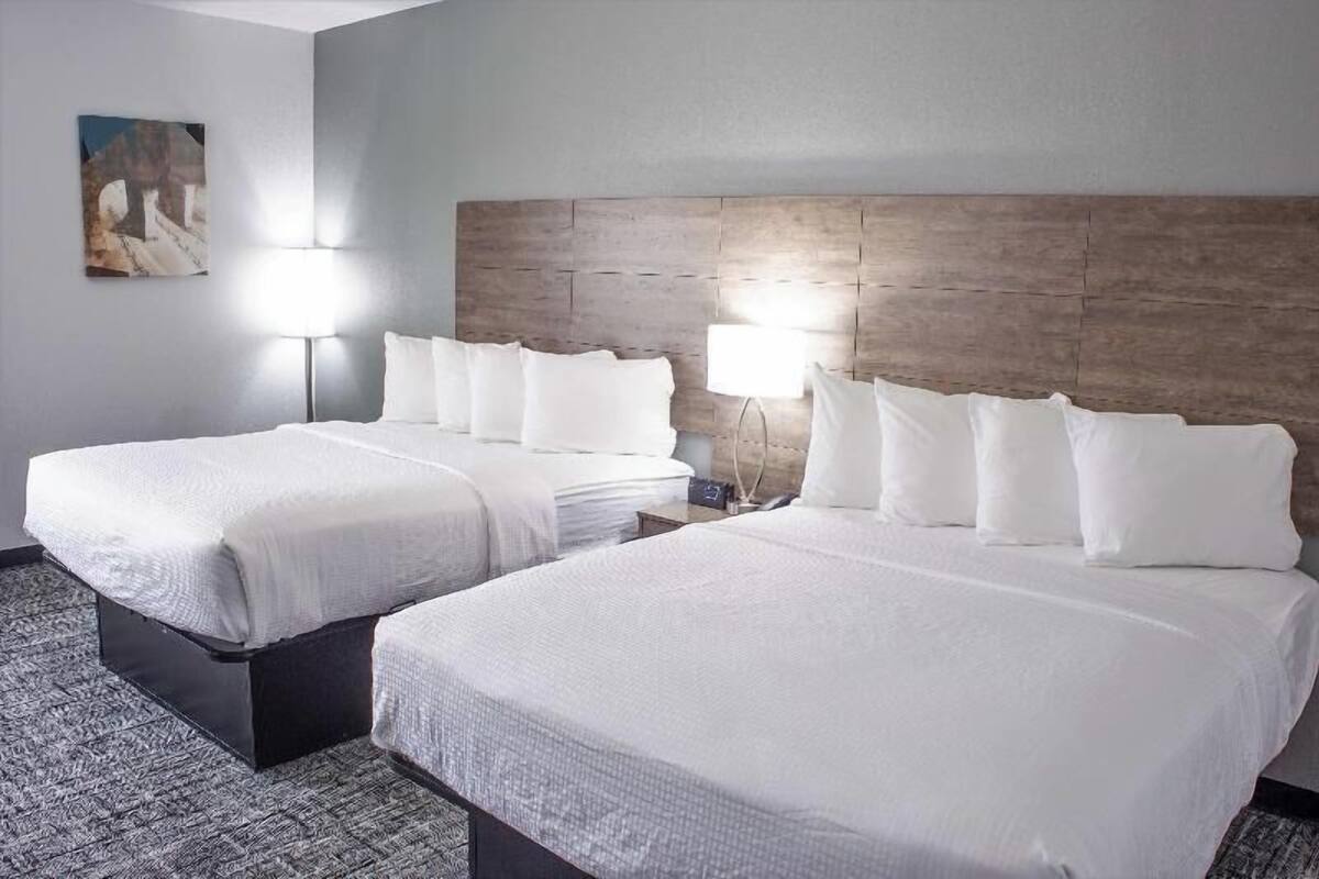 A hotel room with two beds, a wooden headboard, a nightstand with a lamp, and a painting on the wall.