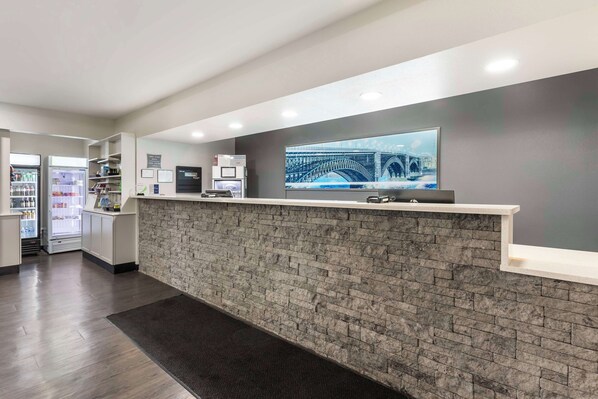 A reception area with a brick wall, a reception desk, a digital screen, and a refrigerator with beverages. - Best Western Plus MidAmerica Hotel (Mascoutah)