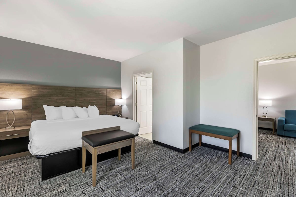 A hotel room with a bed, bedside tables, a bench, a small table, and a chair.