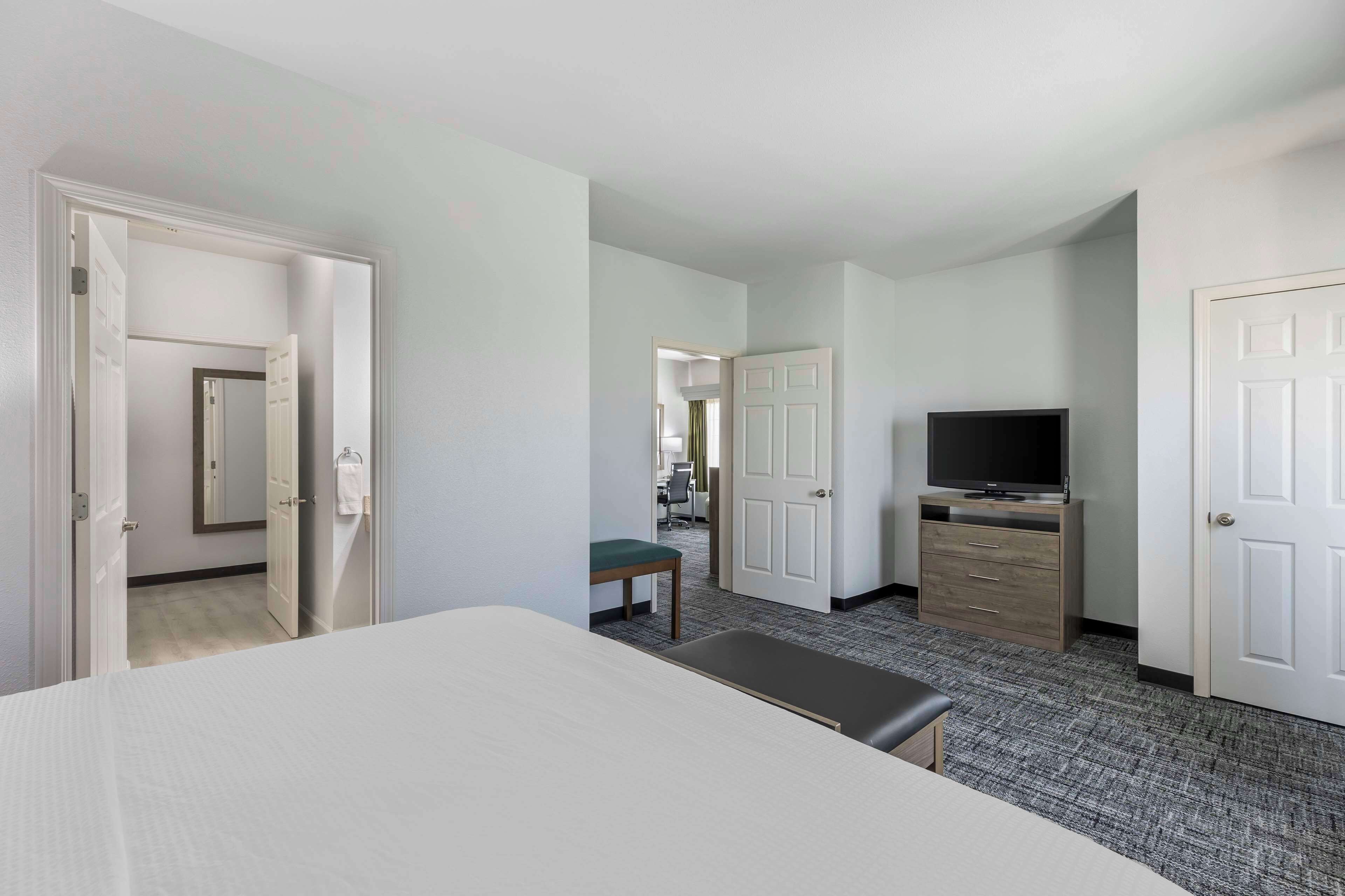 A hotel room with a bed, a bench, a television, a desk, and a wardrobe.