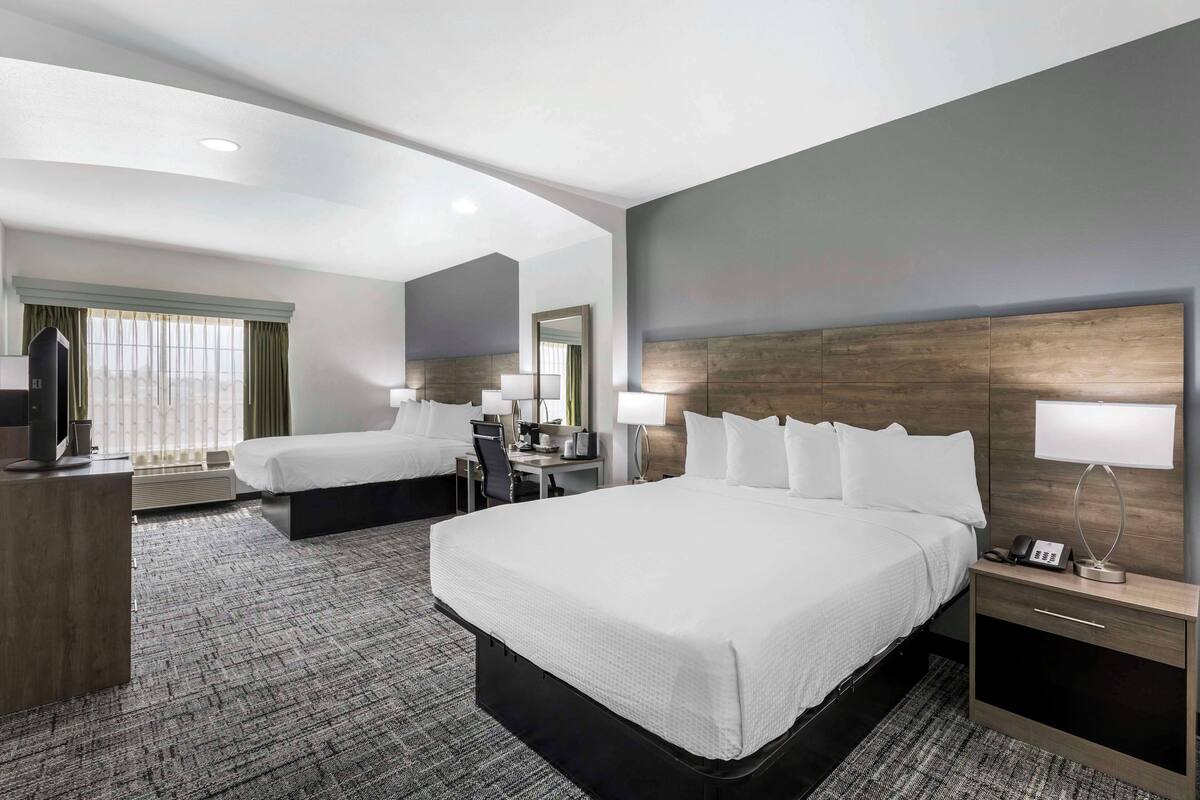 A hotel room with a large bed, a smaller bed, a desk, and a chair.