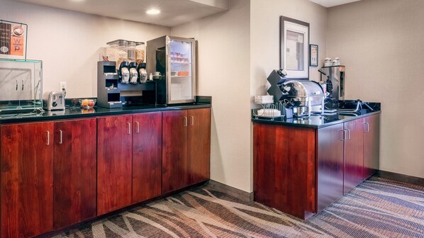 A hotel kitchen with wooden cabinets, a coffee machine, and a refrigerator.