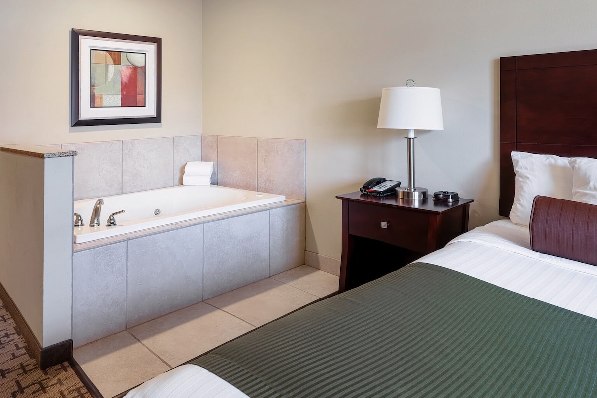 Una habitación de hotel con una cama grande, una mesita de noche con lámpara, un teléfono y una pequeña mesa con cafetera.