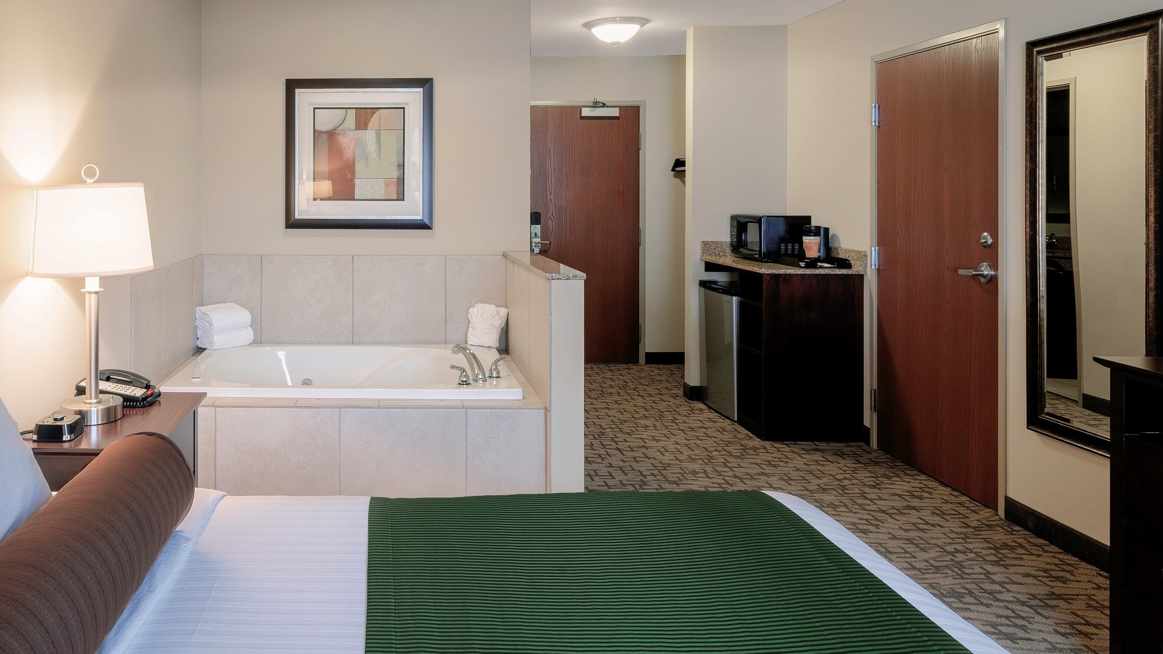 Habitación de hotel con cama, baño con bañera, escritorio con teléfono, cafetera y un cuadro en la pared.