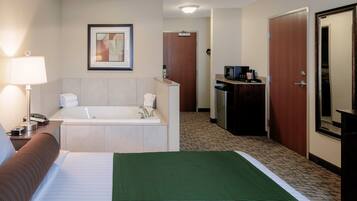 Habitación de hotel con cama, baño con bañera, escritorio con teléfono, cafetera y un cuadro en la pared.