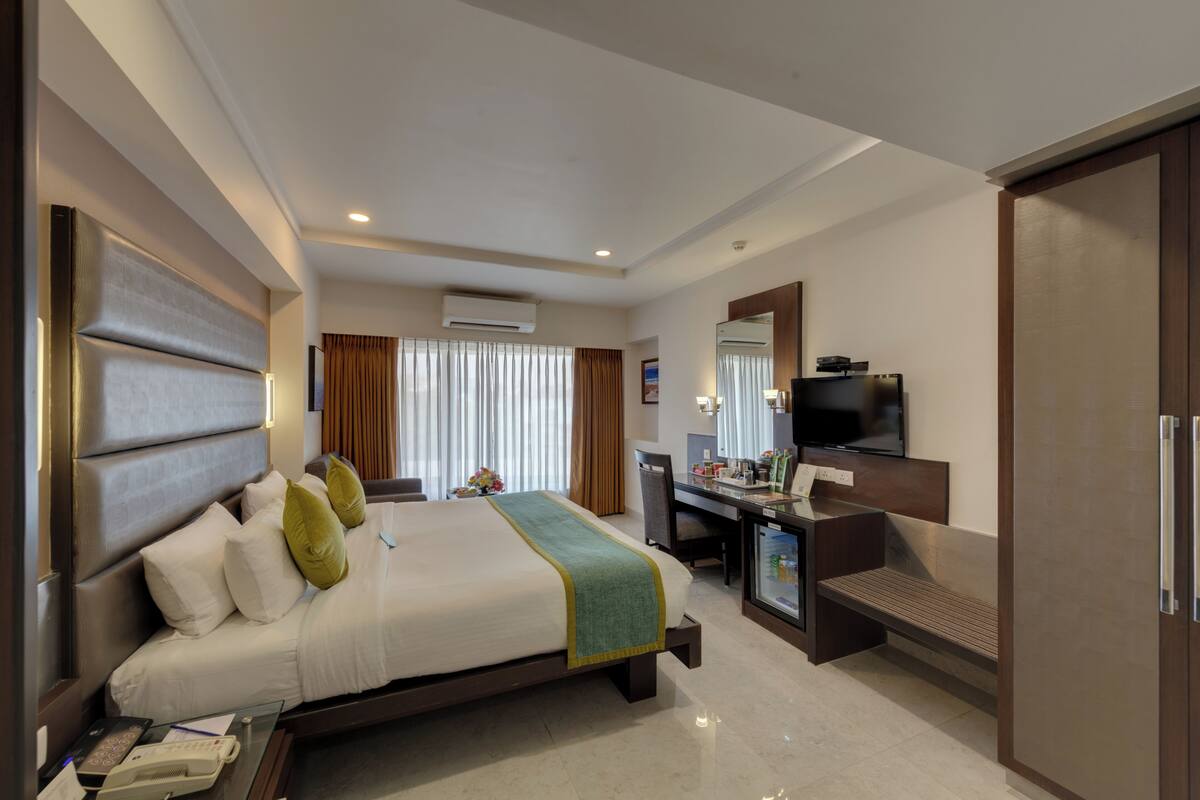 A hotel room with a bed, desk, TV, and a minibar.