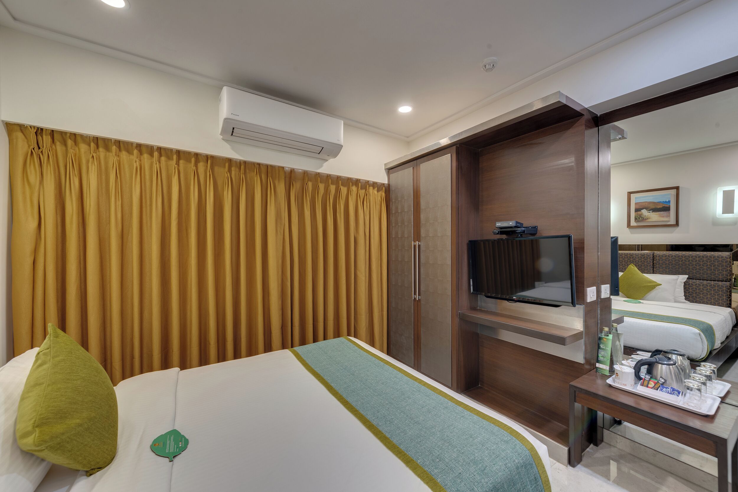 A hotel room with a bed, a television, a desk with a tray of items, and a wardrobe.