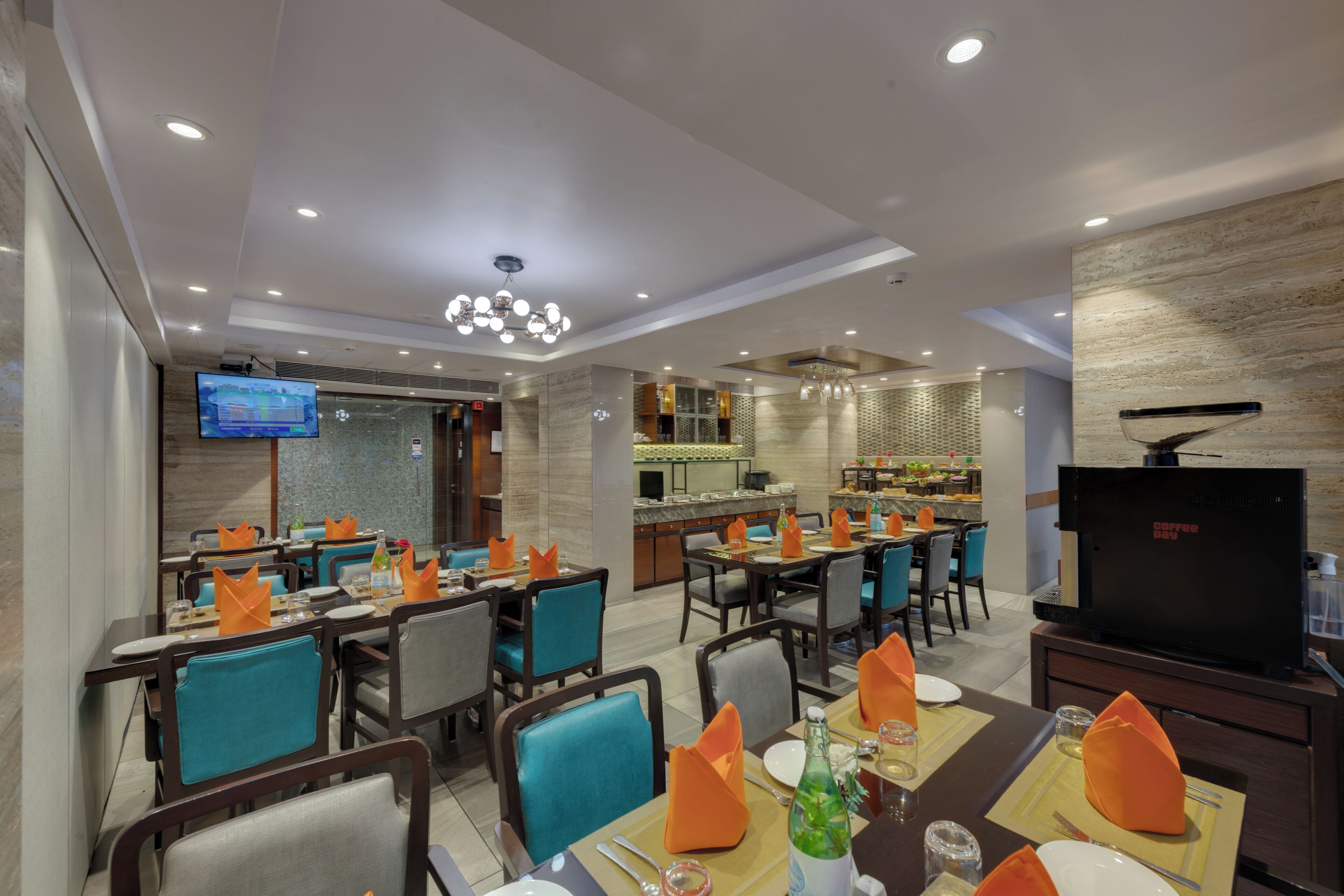 A modern restaurant with multiple dining tables, chairs, and a television screen.