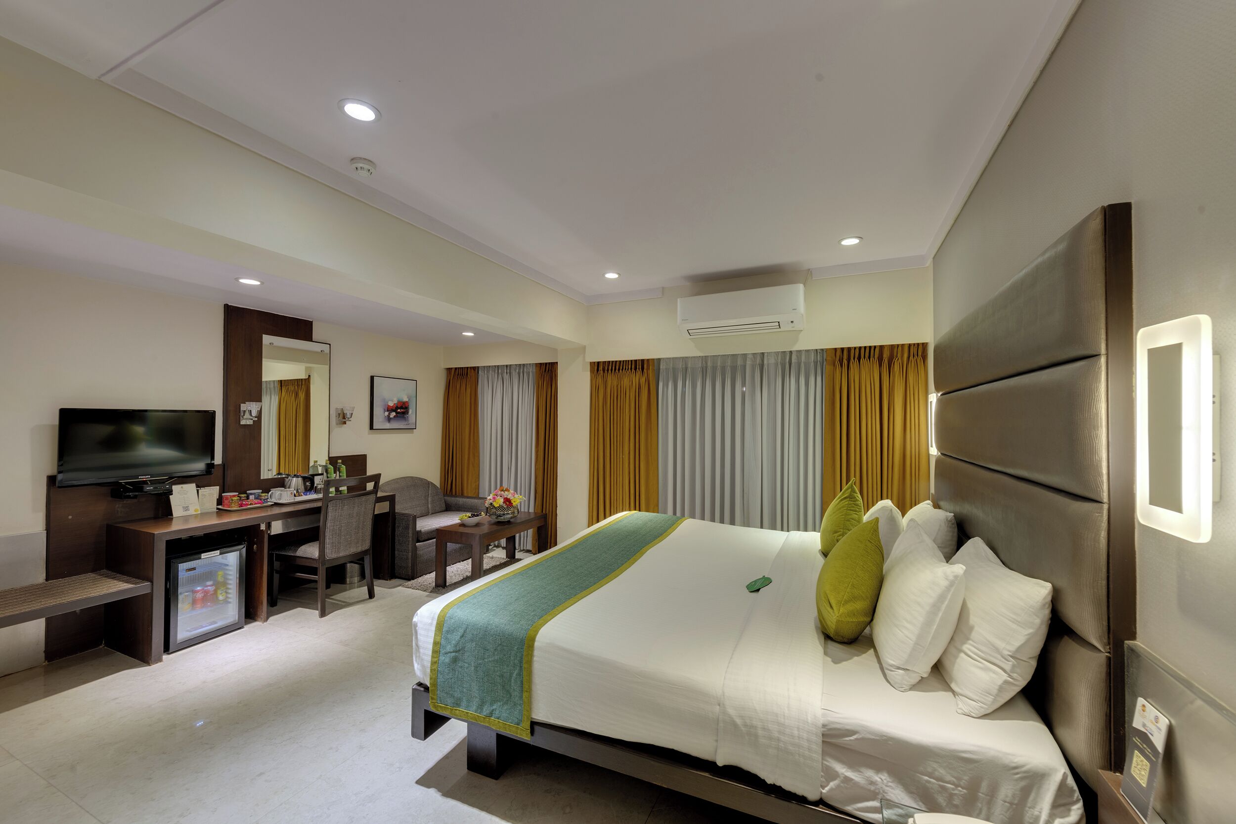 A hotel room with a bed, a desk, a television, and an air conditioning unit.