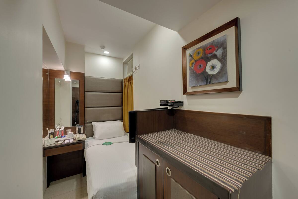 A hotel room with a bed, bedside table, mirror, and a painting on the wall.