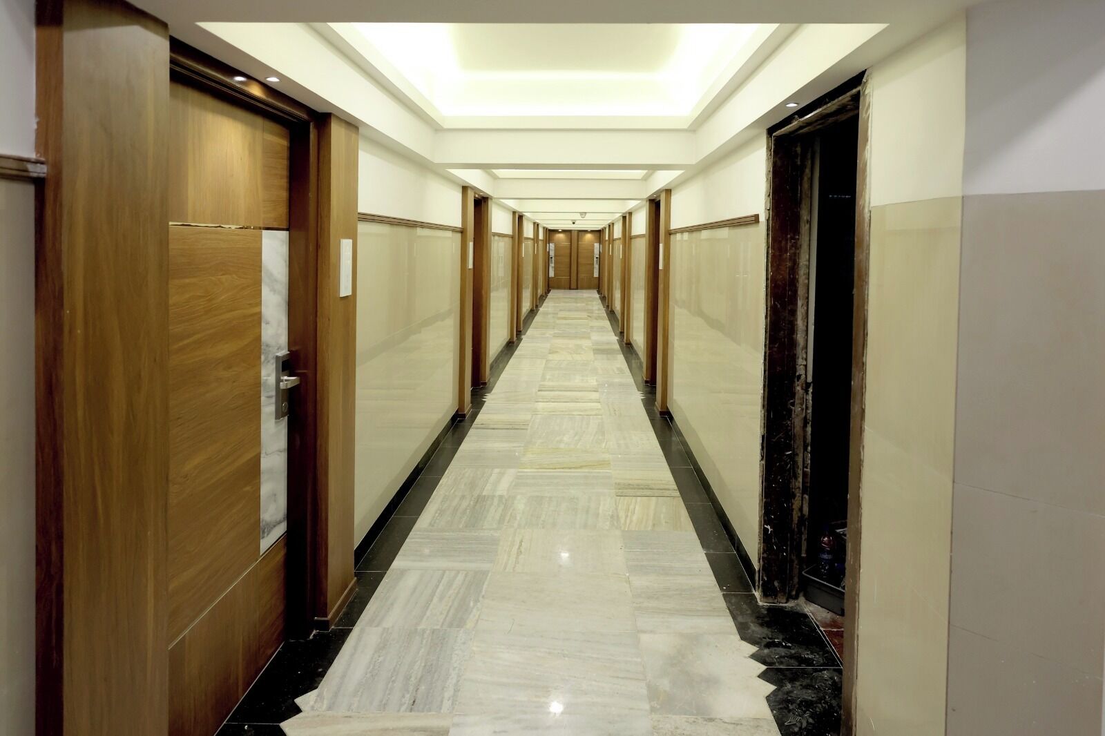 A hotel hallway with wooden doors, marble flooring, and recessed lighting.