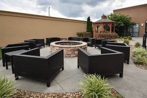 An outdoor seating area with wicker furniture, a stone fire pit, and a gazebo.