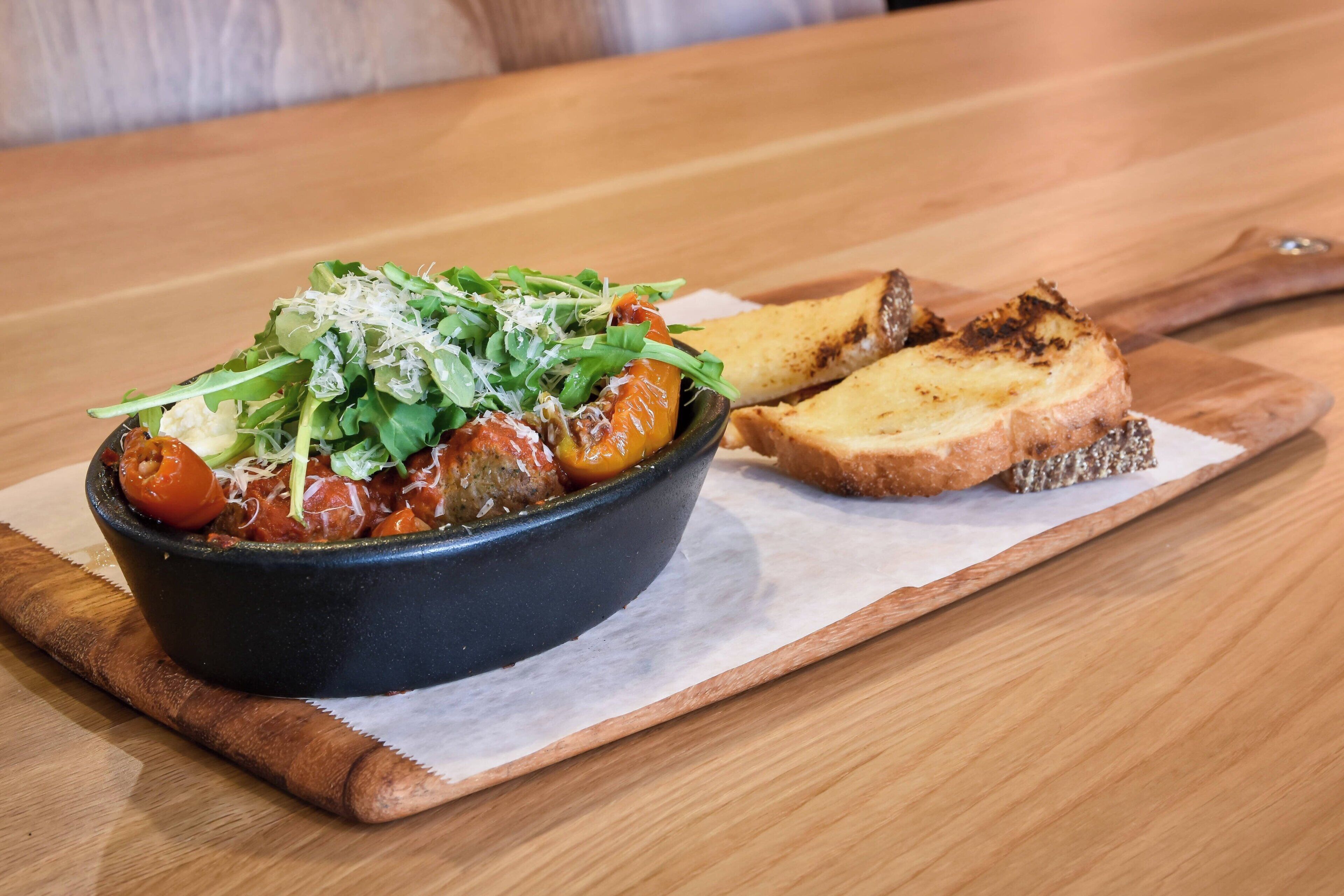 Un plato de comida con una guarnición de pan tostado sobre una mesa de madera.
