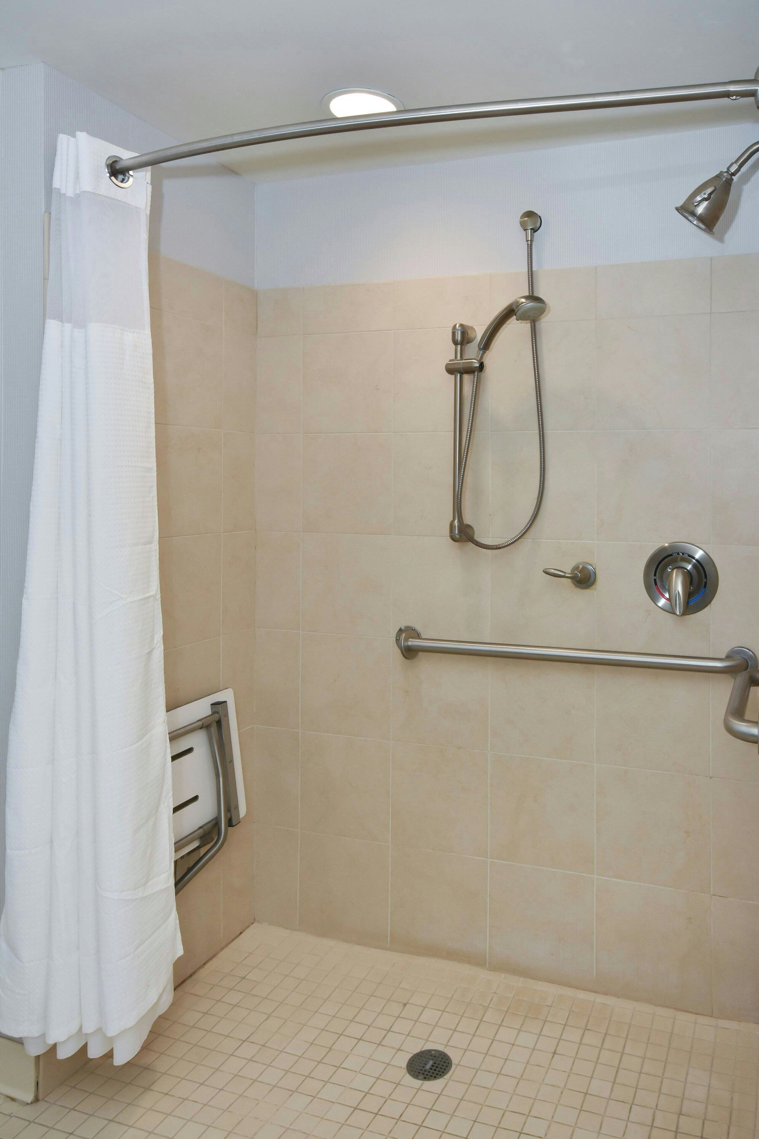 Un espacio de ducha con barra de apoyo, rociador y cortina.