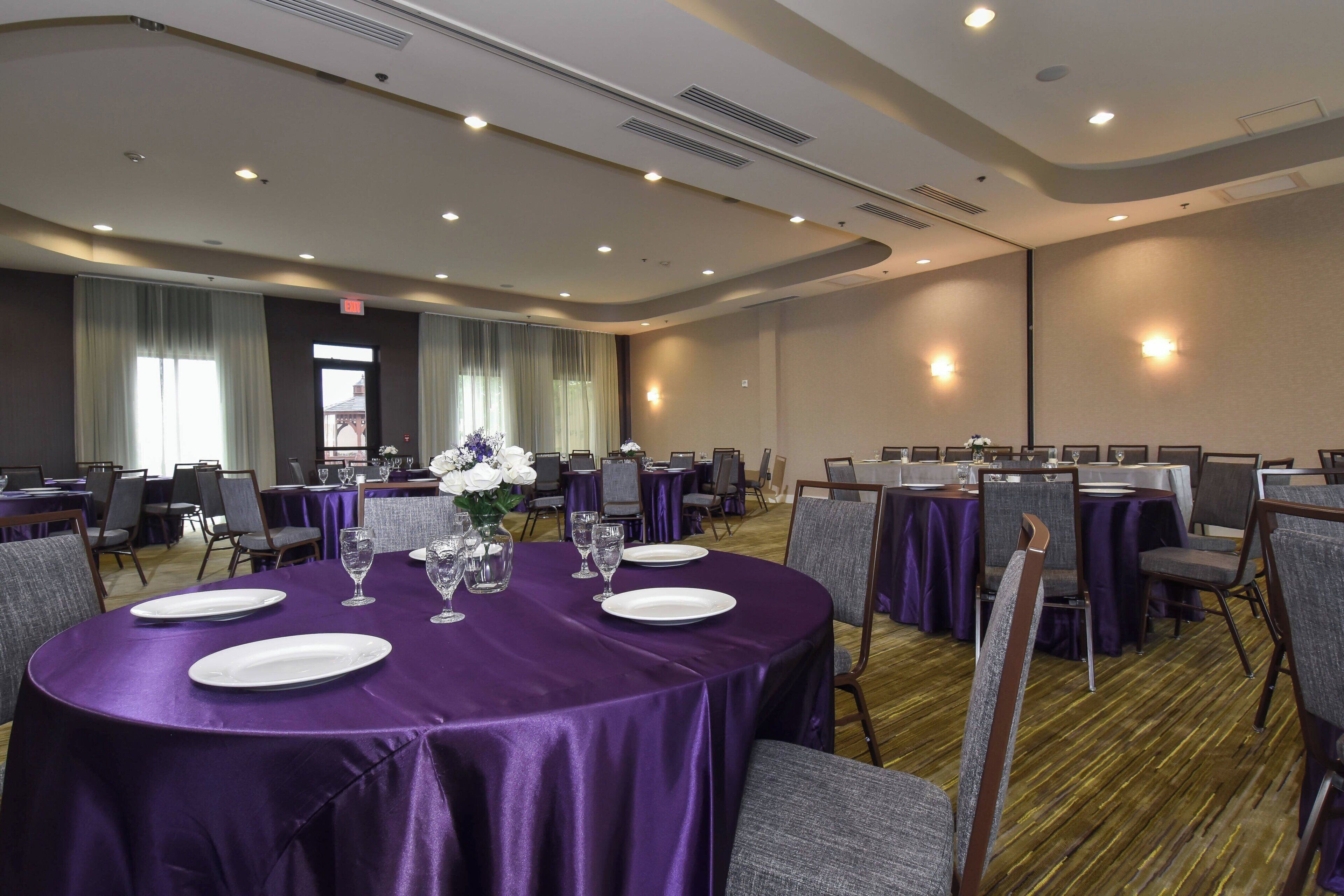 Sala de conferência com mesas redondas, toalhas de mesa roxas e cadeiras.