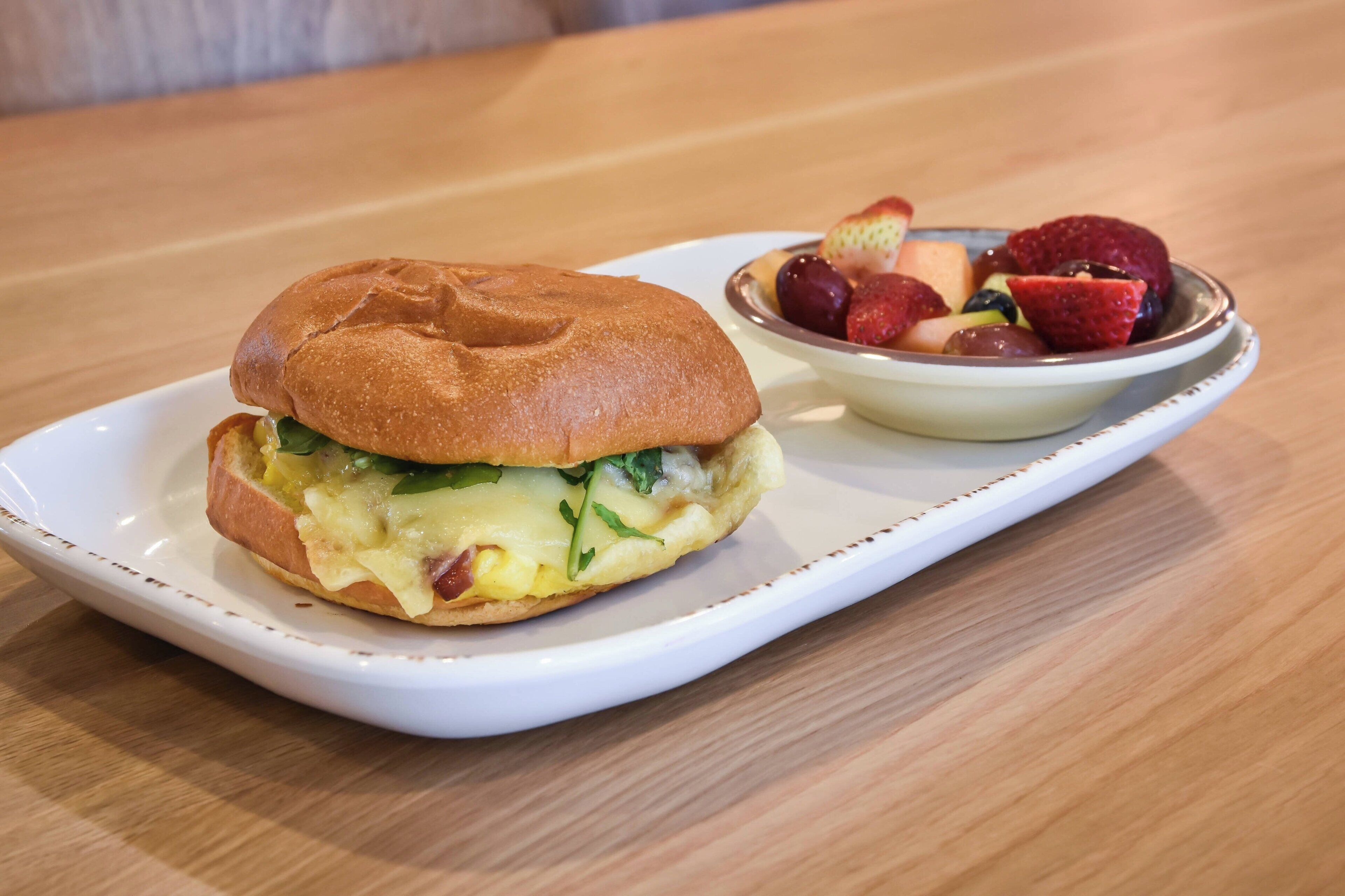 A sandwich on a white plate with a side of fruit.
