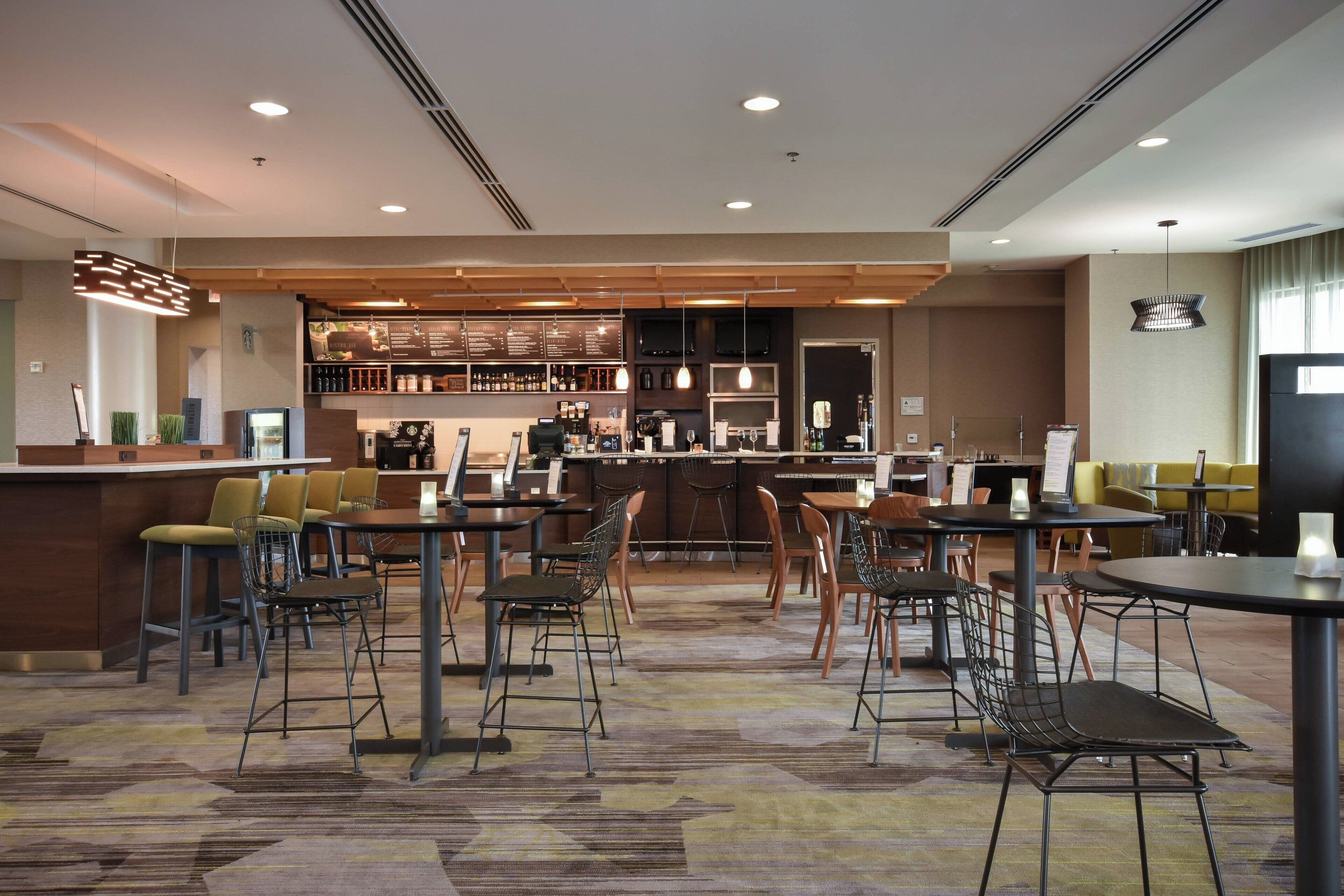 A modern hotel lobby with a bar area, seating arrangements, and a carpeted floor.