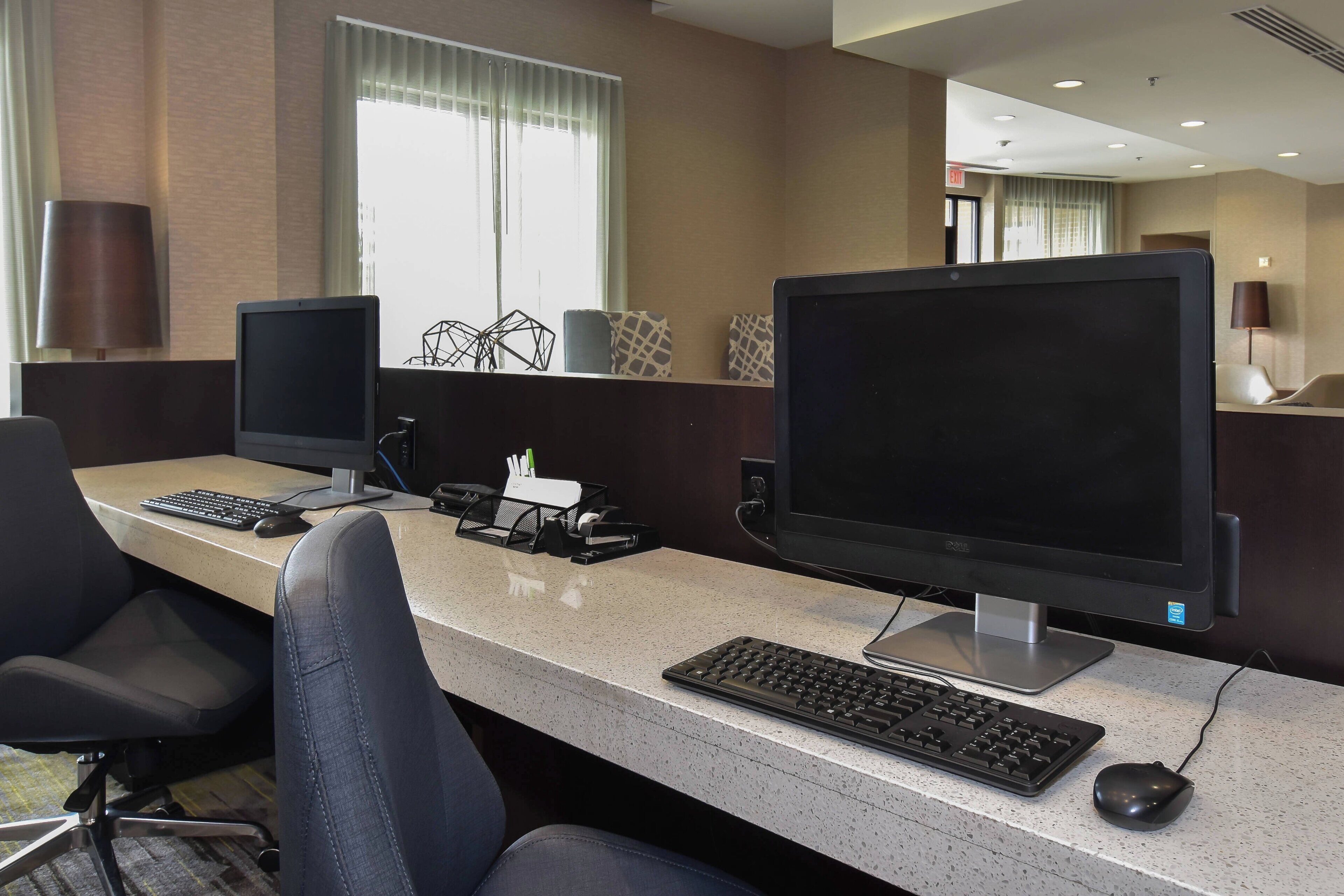 Un espacio de trabajo en un hotel con dos monitores de computadora, un teclado, un ratón y sillas de oficina.