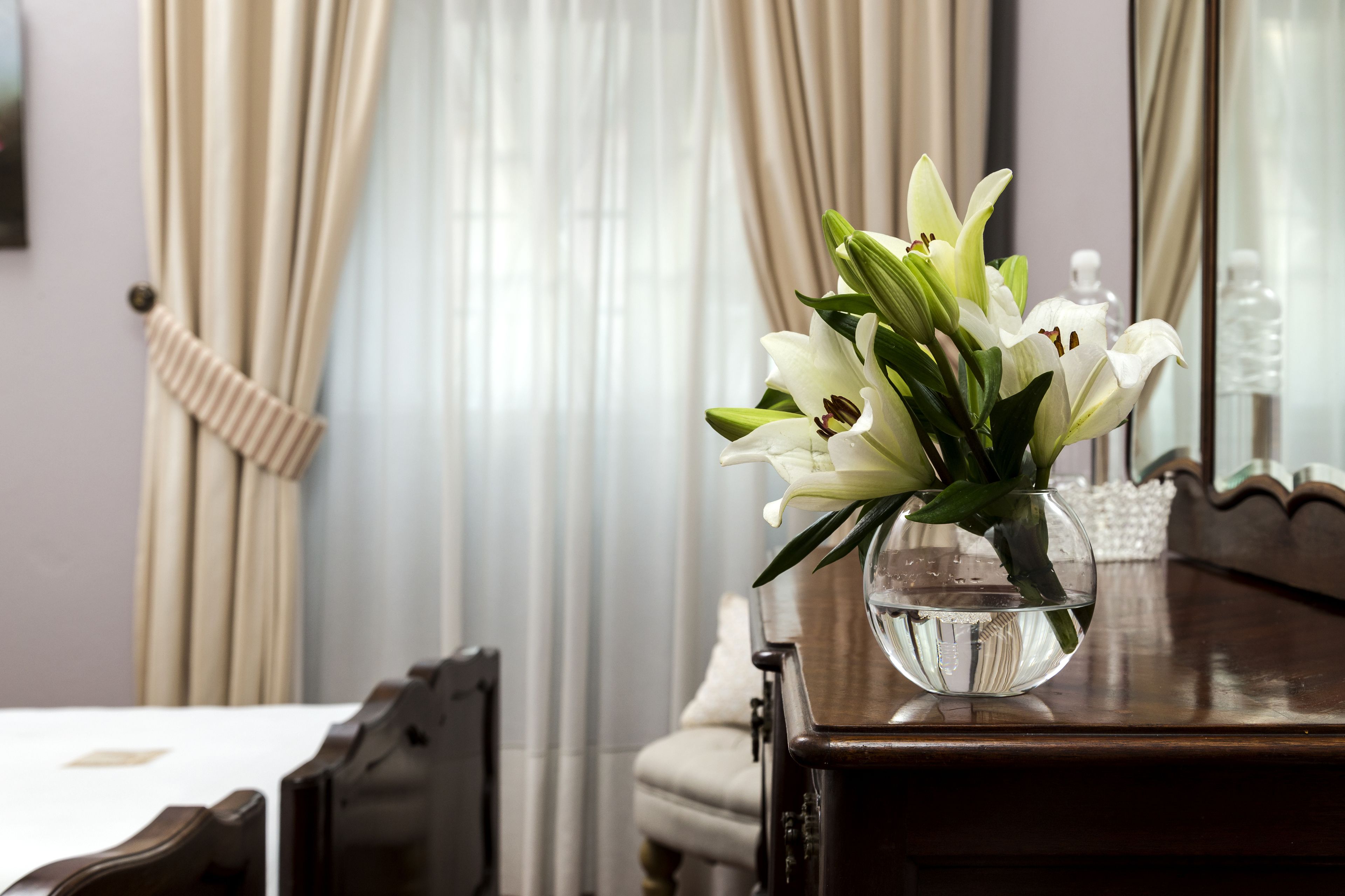 A wooden table with a clear vase containing white lilies.