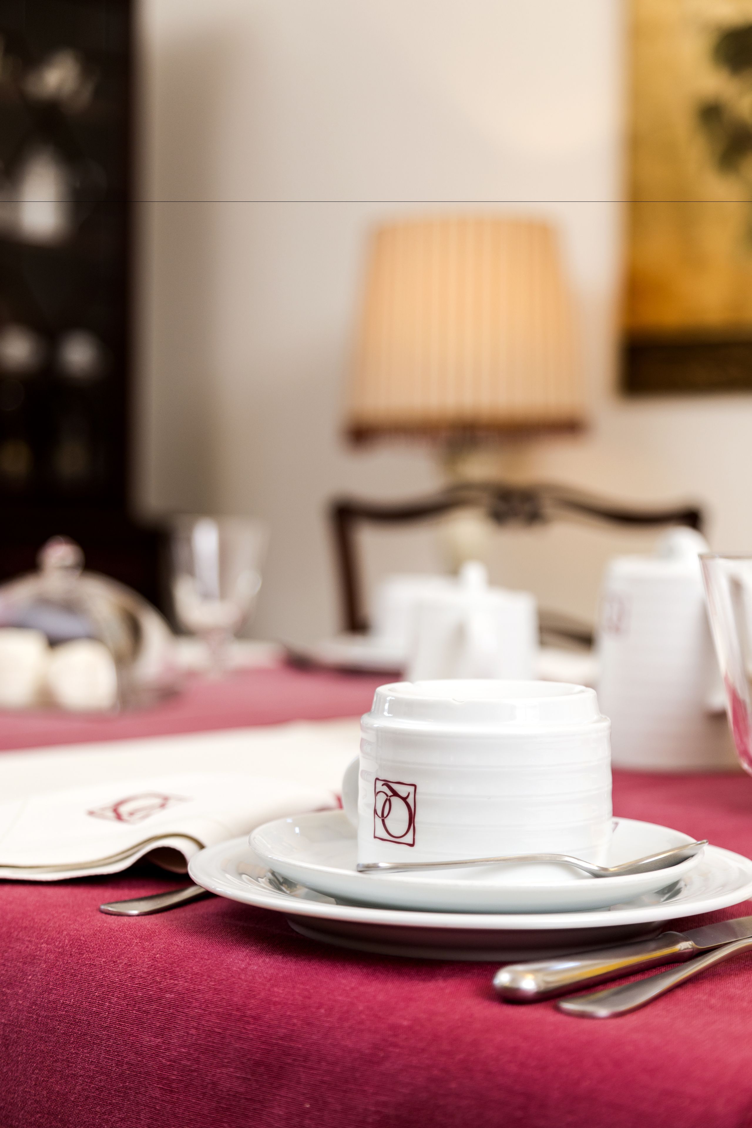 A table set with white teacups, saucers, and silverware on a red tablecloth.