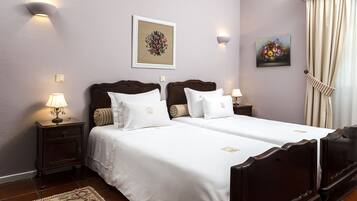A hotel room with two beds, a nightstand with a lamp, a framed floral artwork, and a painting of flowers.