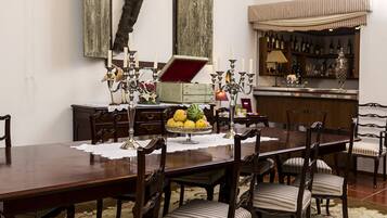 Un comedor con una mesa de madera, seis sillas, una araña y una zona de bar al fondo.