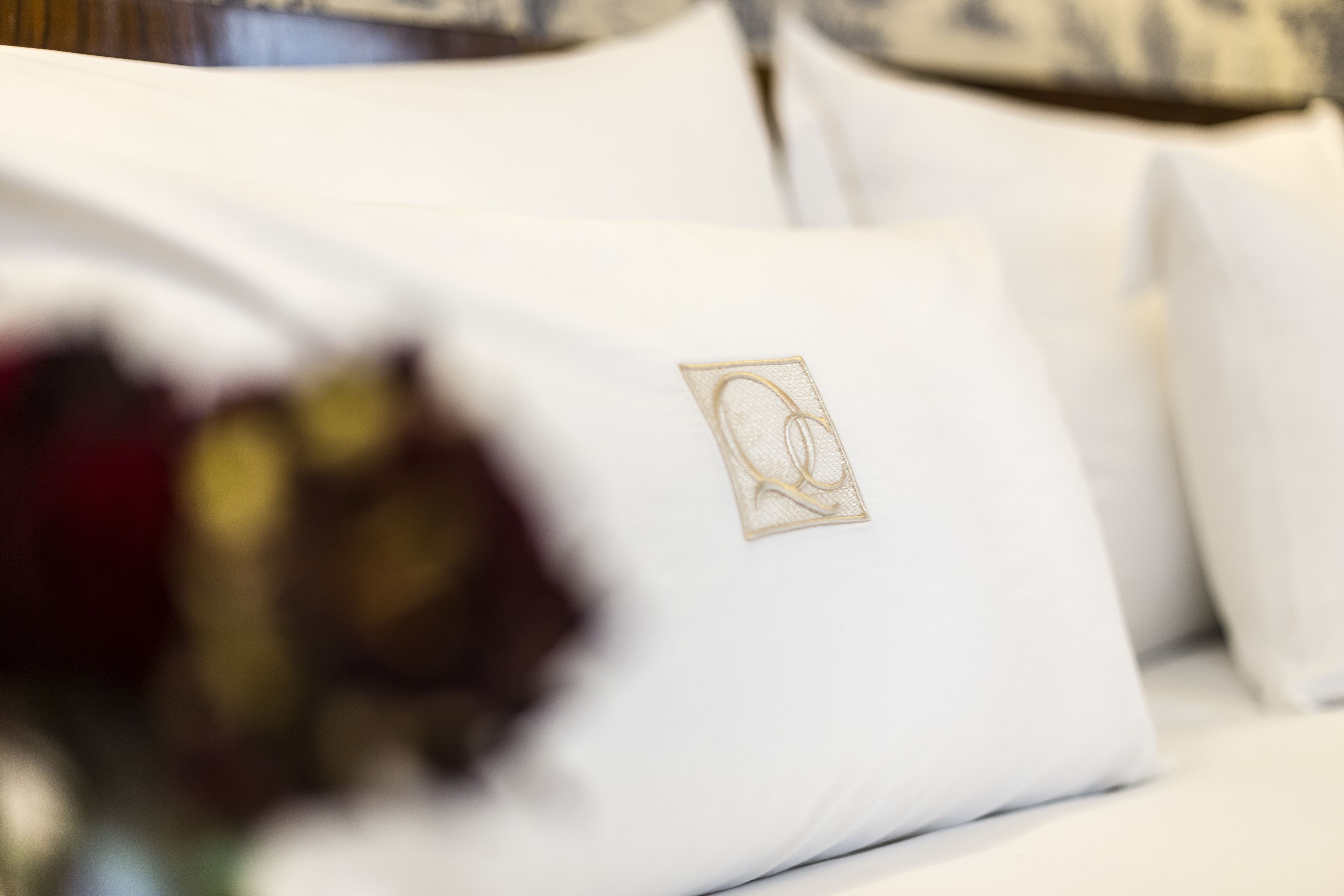 Primer plano de un almohadón blanco con un logotipo bordado en dorado sobre una cama.