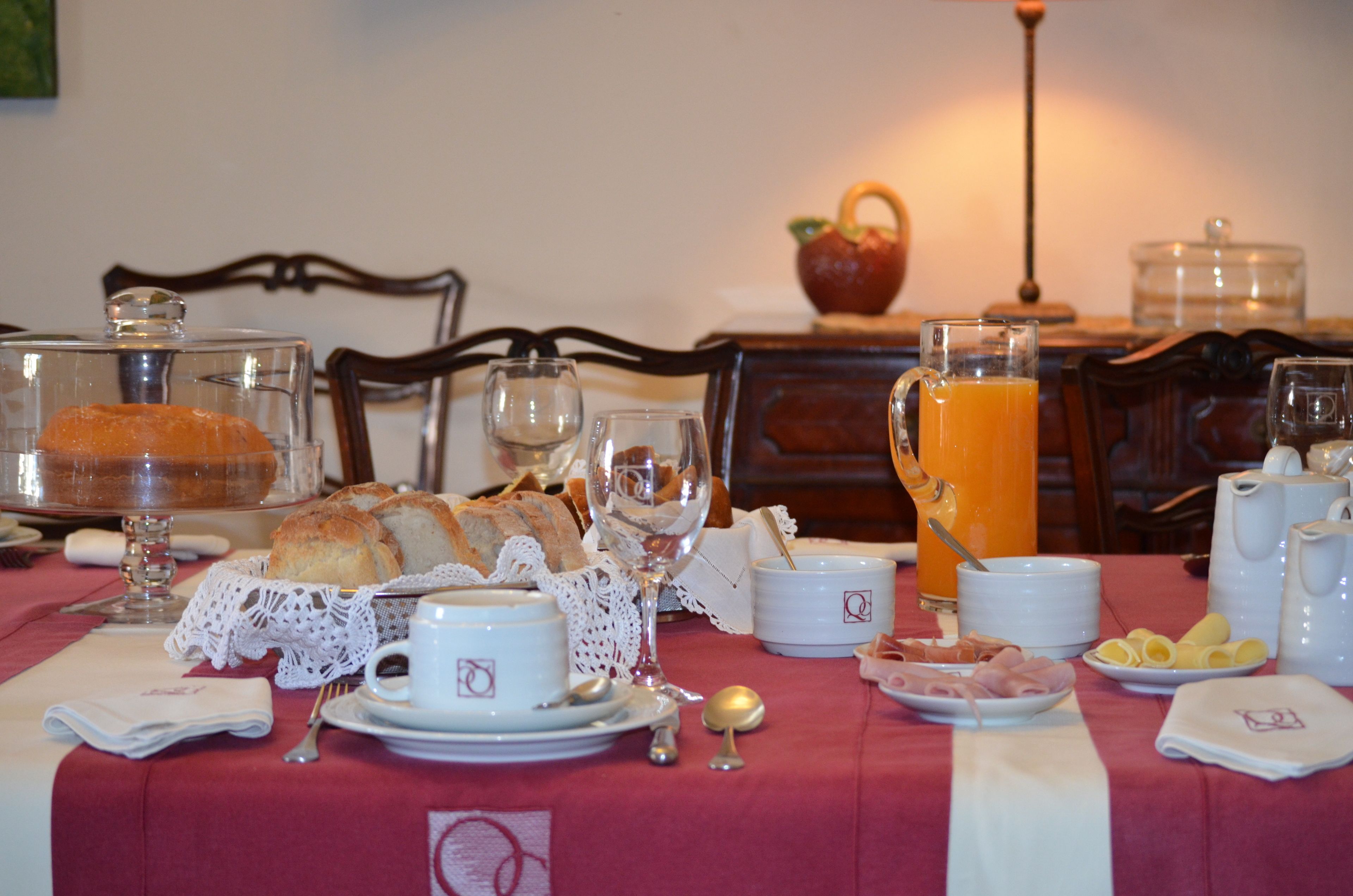 Une table de petit-déjeuner dressée avec du pain, des viennoiseries, des tasses de café et un verre de jus d’orange.