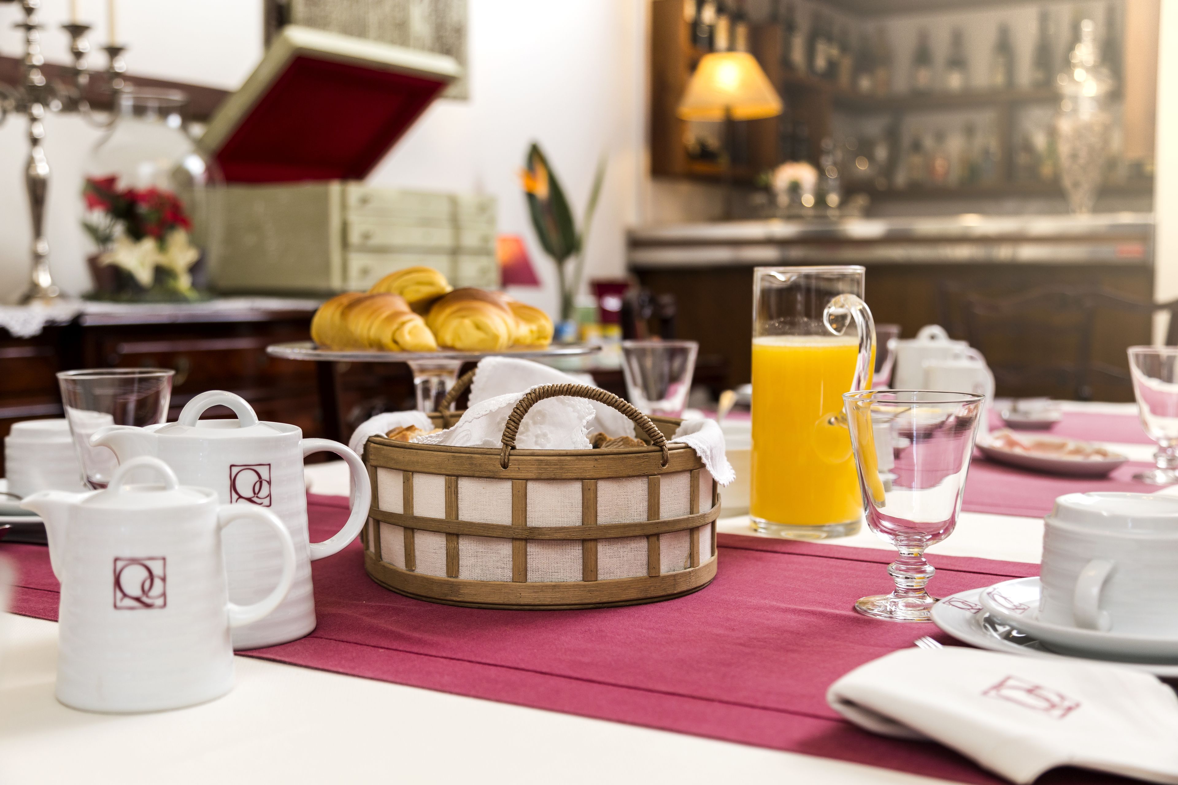Desayuno con croissants, una cesta, una jarra de zumo de naranja y tazas blancas con un logotipo.