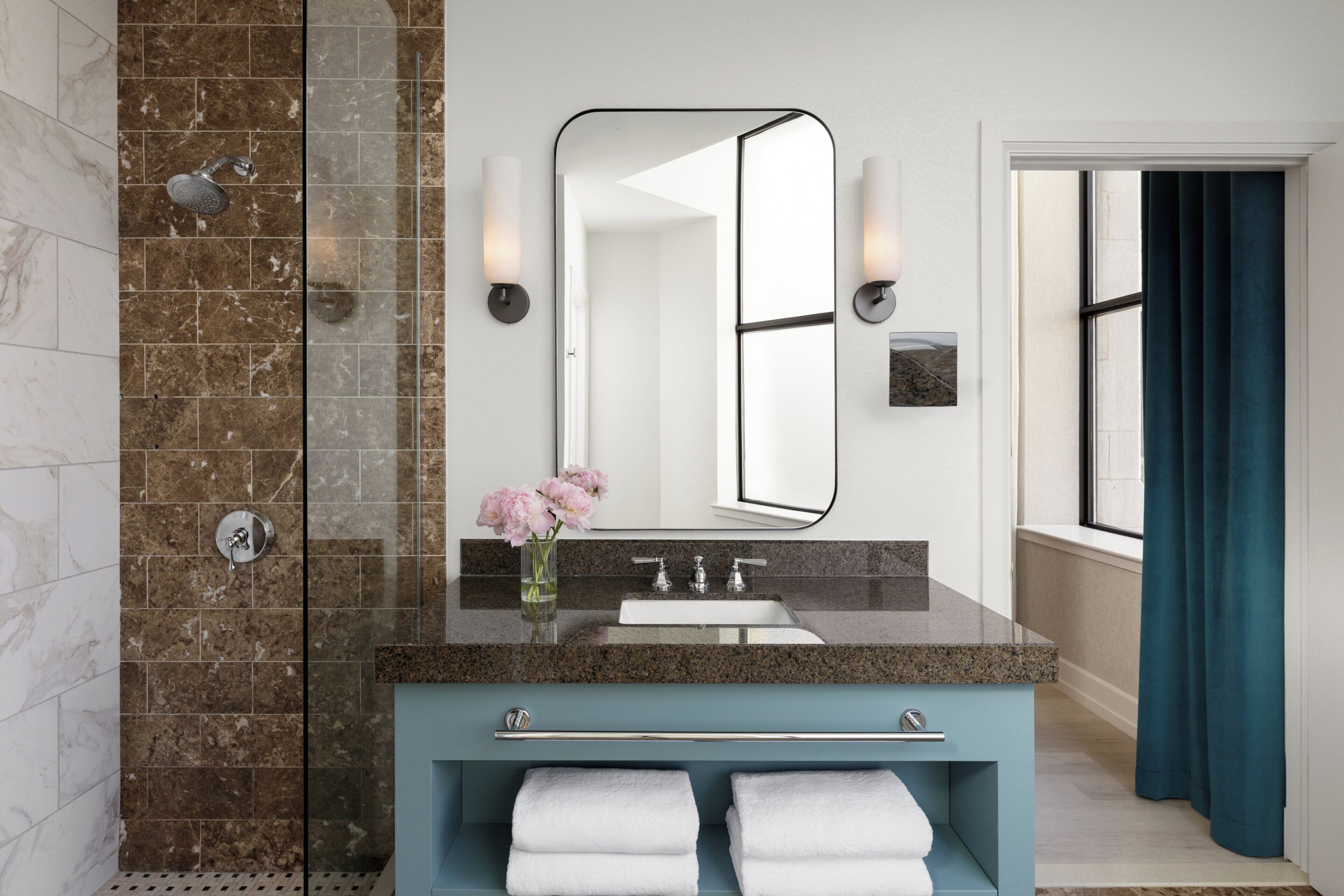 A bathroom with a glass-enclosed shower, a sink with a marble countertop, a mirror, and a towel rack.