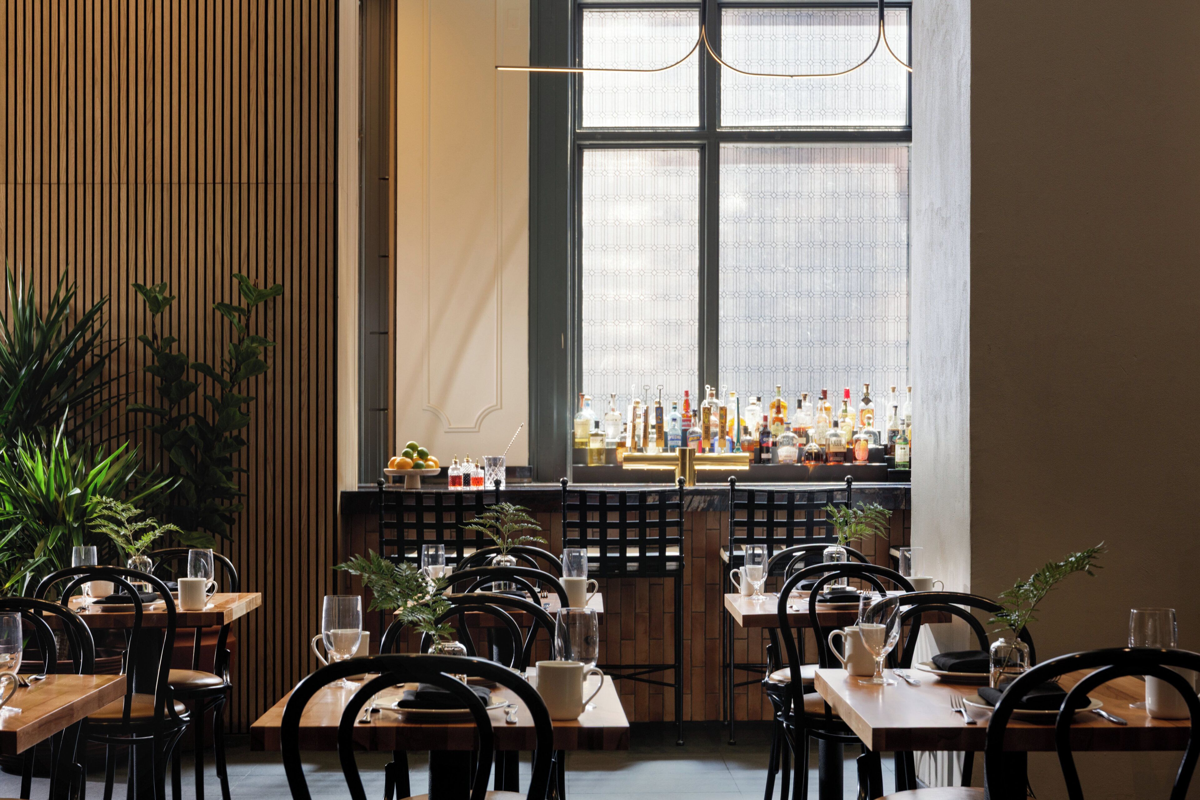 Un restaurant avec de nombreuses tables et chaises, un bar bien garni de bouteilles et une grande fenêtre offrant une belle vue.