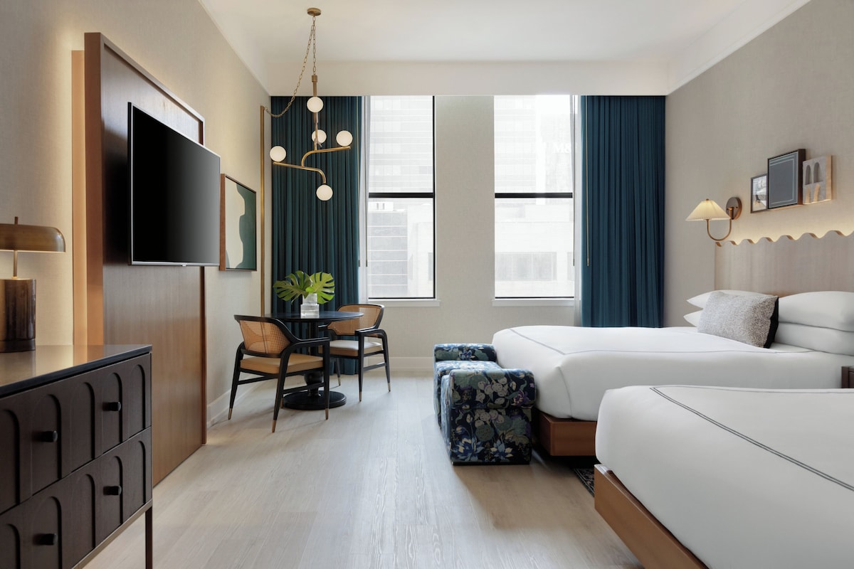 A hotel room with a bed, a desk, a chair, a TV, and a window.